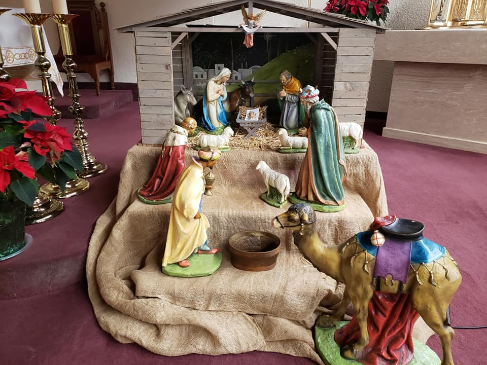a layered Nativity scene with a kneeling King and 2 standing kings facing the Christ Child, His mother Mary and Joseph in the stable- a few random sheep look on as well as a well dressed camel siting in the front