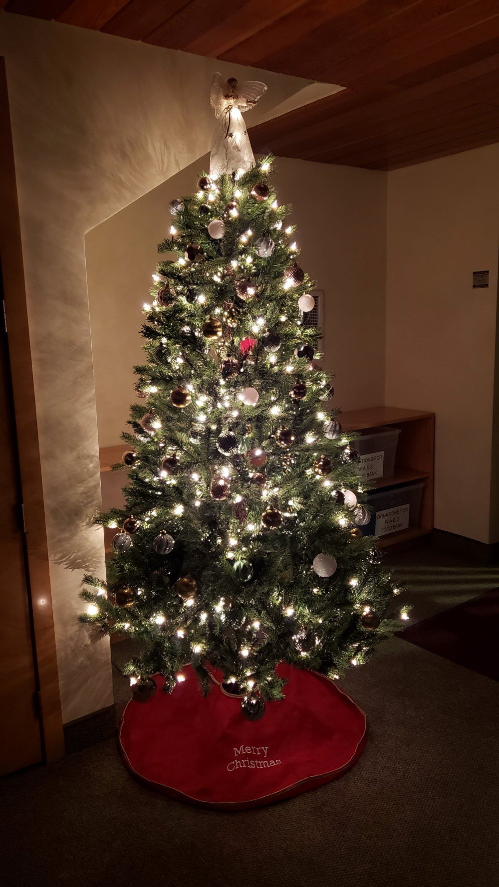 A pine tree decorated with silver and gold balls, white lights and a white angel on top